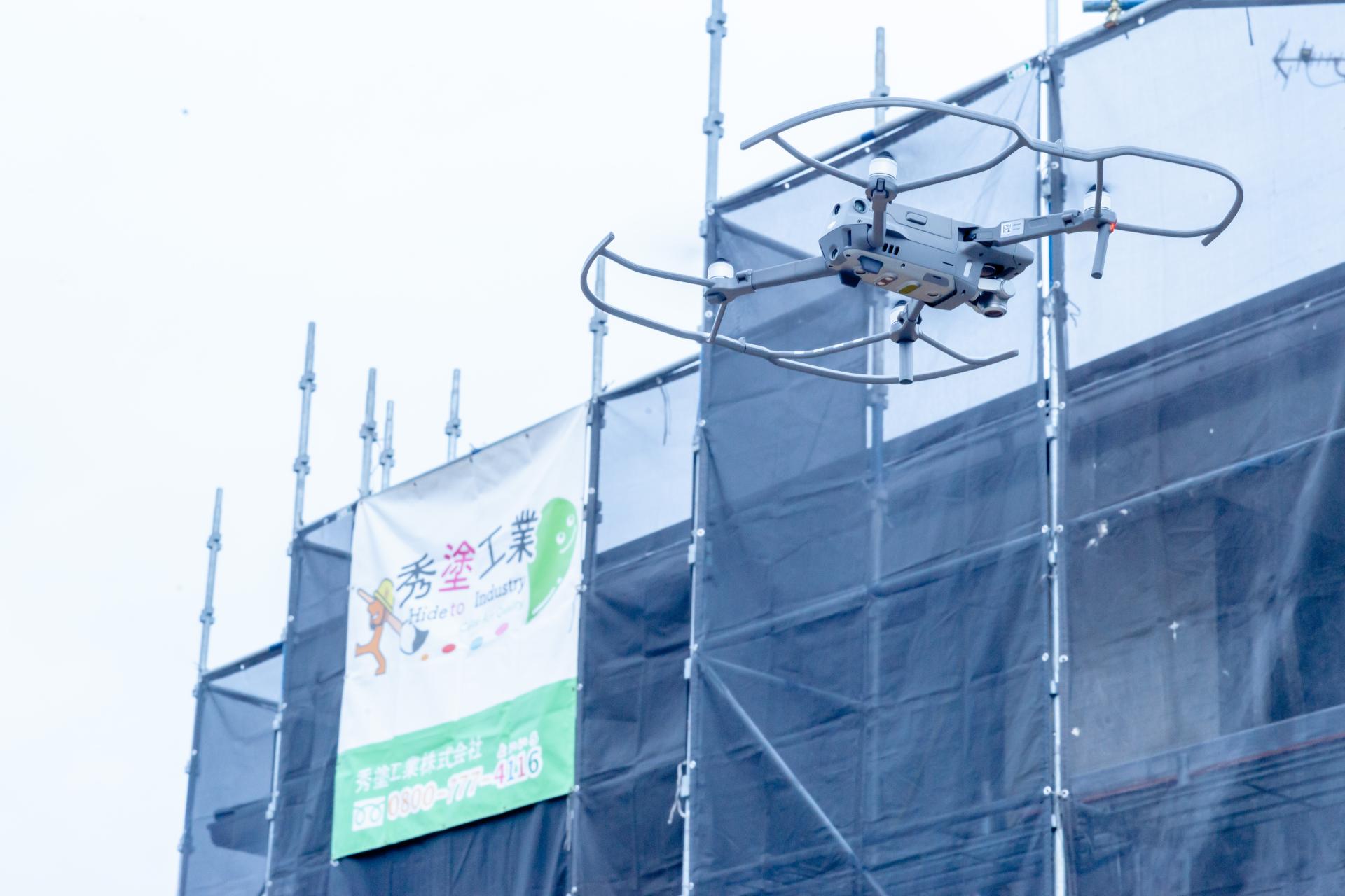 足場に囲まれた建物をドローンで空撮調査している様子